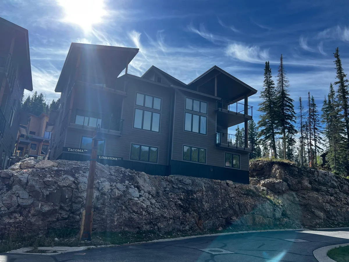 This exterior image highlights the modern architectural design of the property, with large windows reflecting sunlight and balconies overlooking the natural landscape. The contemporary building stands out amidst the surrounding beauty, suggesting a blend of luxury and nature.