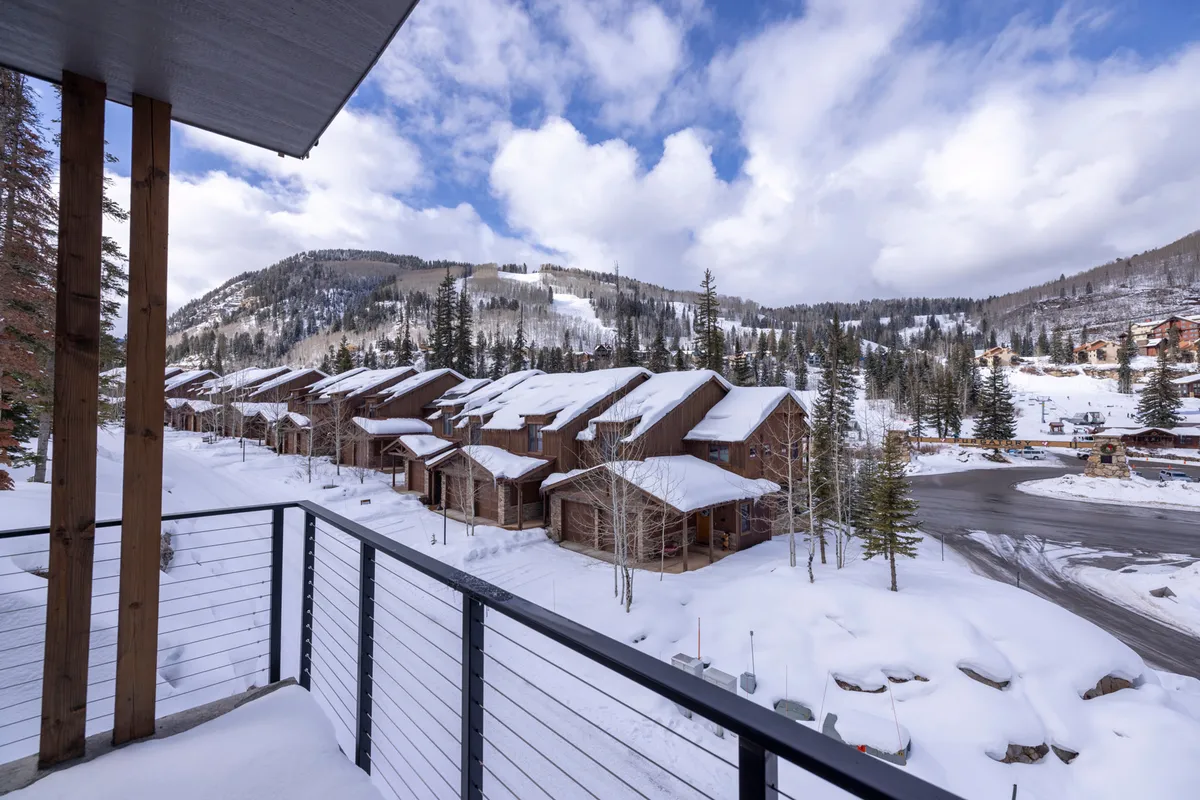 This exterior image showcases snow-covered rooftops nestled among pine trees, with a stunning mountain landscape in the background. The scene captures the tranquil, wintry environment surrounding the property, conveying the proximity to the slopes and the inviting atmosphere of a ski retreat.