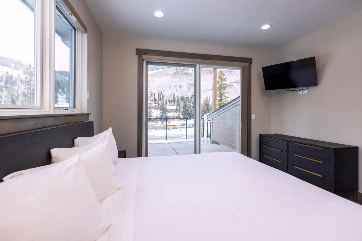 A cozy bedroom scene featuring a plush bed, large windows, and a door leading out to a patio—inviting the outdoors in and highlighting the tranquil connection between indoor comfort and the natural surroundings.