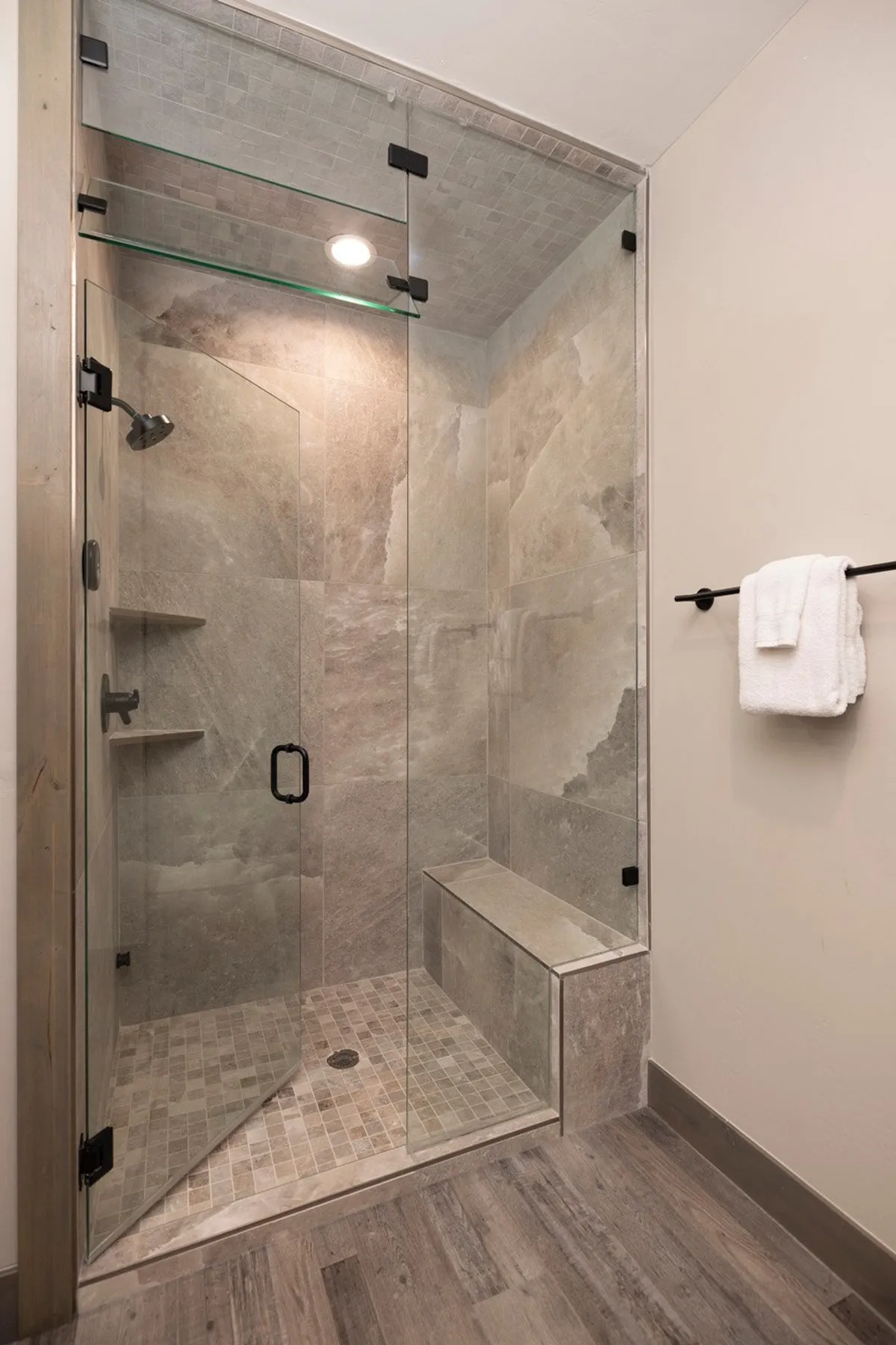 A serene, spa-inspired bathroom with a glass shower enclosure, textured stone tiles, and a built-in bench. The space exudes calm sophistication and invites guests to unwind with a soothing steam shower after outdoor activities.
