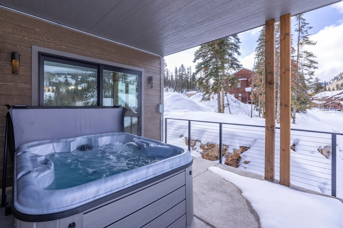 A serene exterior shot of a hot tub framed by wooden pillars and surrounded by a snow-covered landscape, inviting relaxation after a day on the slopes. The scene hints at the unique mountain retreat experience and the opportunity to unwind in the fresh alpine air.