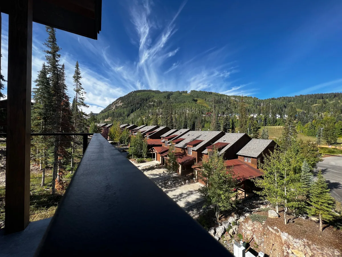 A sweeping exterior view of the property with rows of homes set against a dramatic mountain range and lush greenery, under a wide blue sky. The environment is vibrant and hints at nearby trails and outdoor possibilities.
