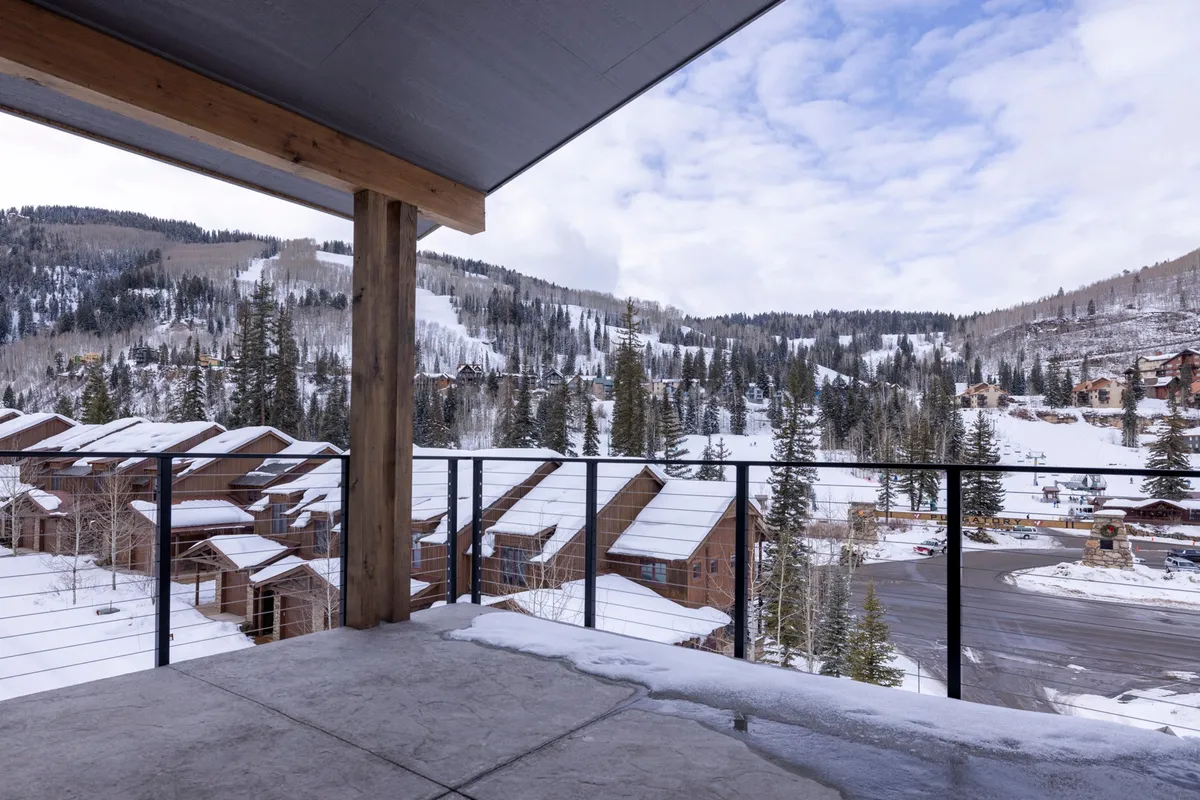 An inviting exterior scene featuring snow-covered mountains, cozy wooden cabins, and a balcony railing. The atmosphere is tranquil, evoking the charm of winter adventures and the enjoyment of peaceful moments outdoors.